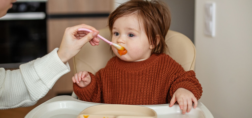 Toddler girl in brown sweater eating delicious pumpkin puree