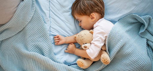 Toddler boy sleeping in blue sheets with a teddy bear