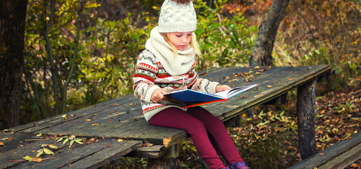 Little Girl Sitting on the bench reading a book in fall