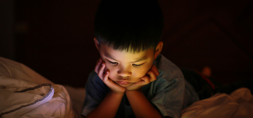 Asian toddler boy watching his tablet screen in bed at night