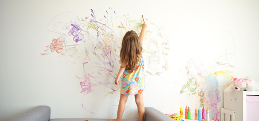 toddler painting on a white wall with crayons